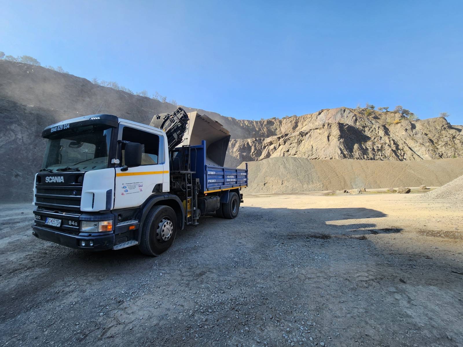 Truck positioned beside bulk construction material in a quarry.