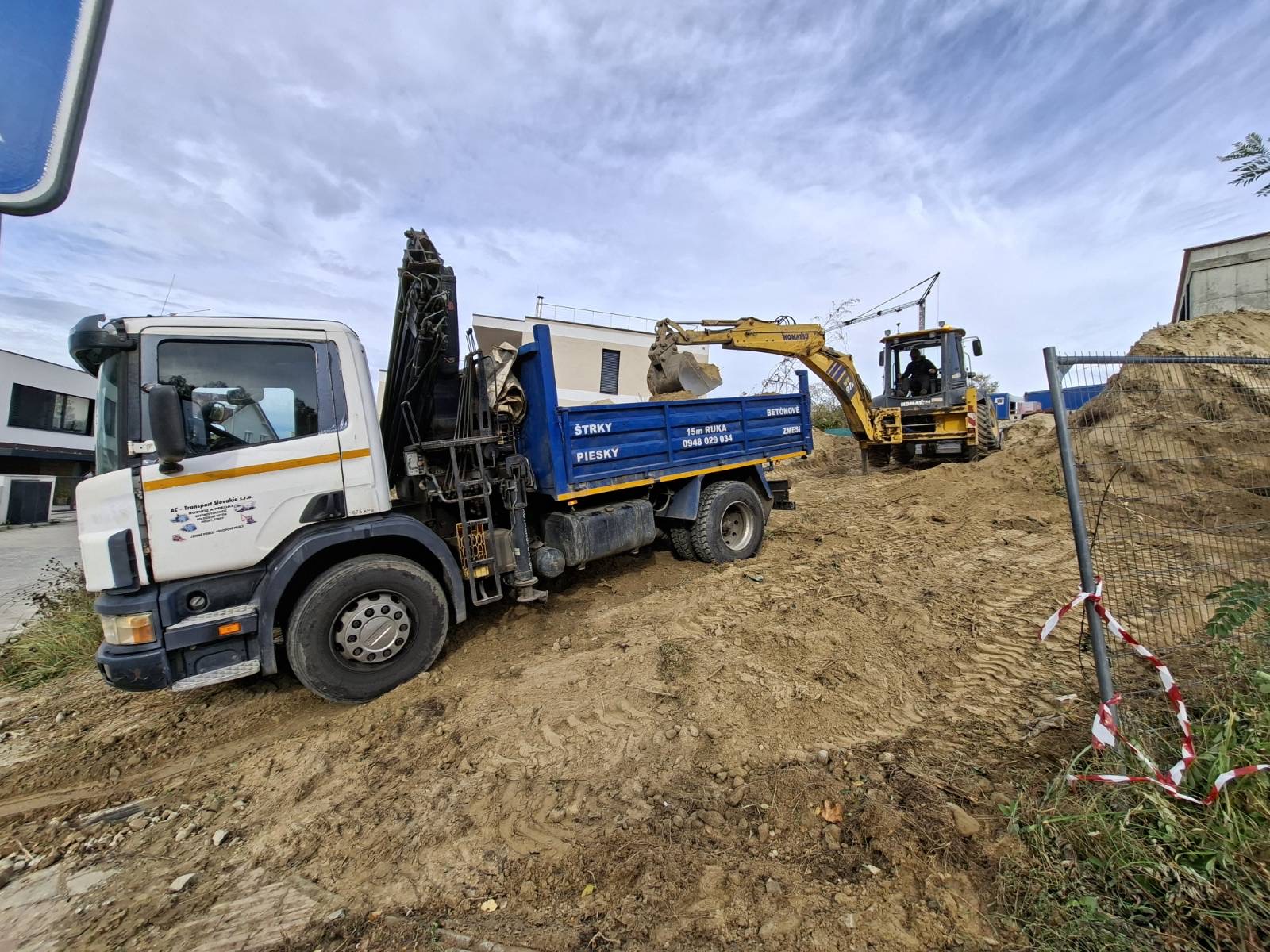 Truck beside excavated soil and bulk material on a worksite.