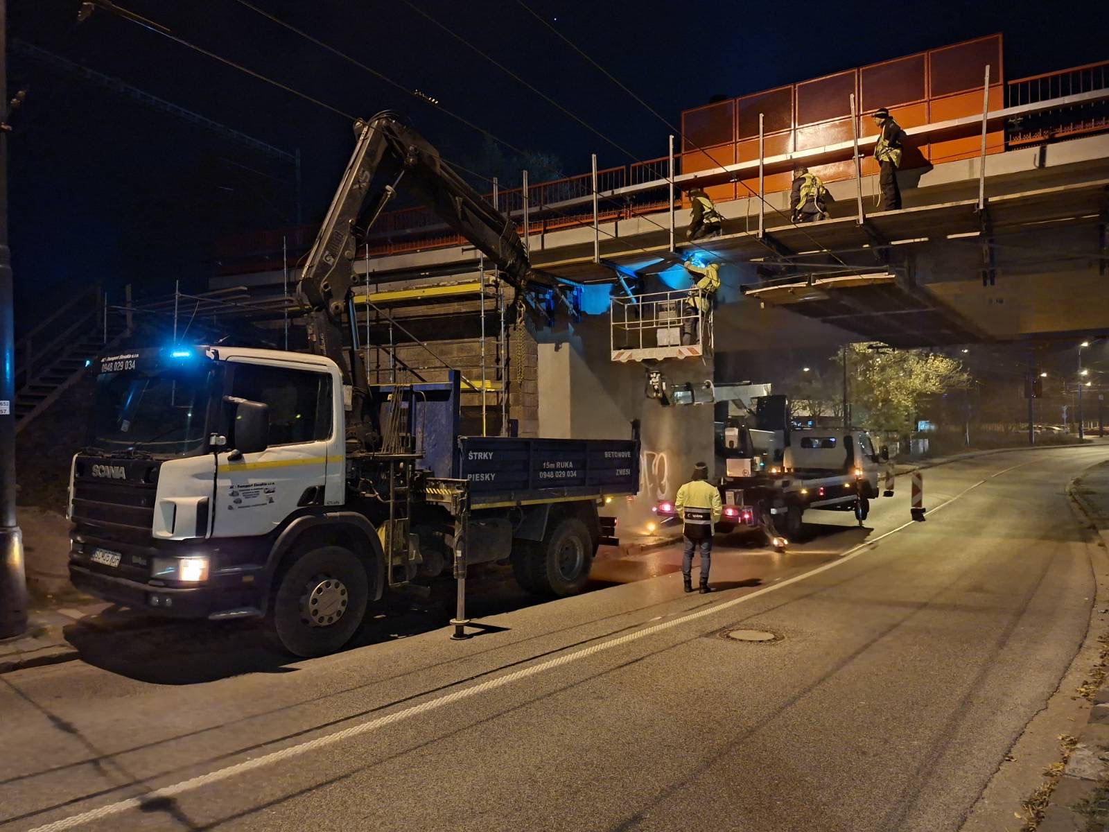 Truck with a hydraulic crane working at night beside a bridge.